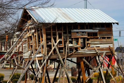 A dilapidated wooden structure on stilts, with a metal roof, surrounded by a barren landscape and utility poles.