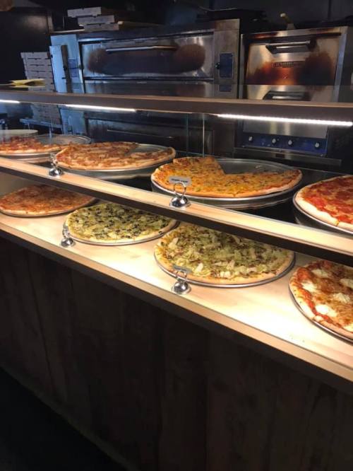 A display of various pizzas on trays, including different toppings, in a restaurant setting.