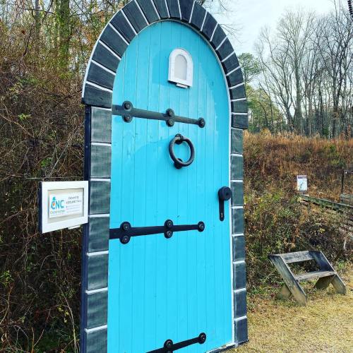 A large, blue wooden door with black accents and a knocker, set in a natural outdoor environment.