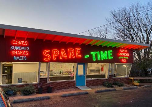 Brightly lit storefront of "Spare-Time" featuring neon signs for ice cream, coffee, and snacks at dusk.