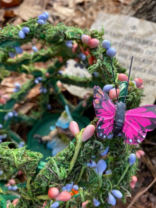 A decorative wreath made of green foliage and colorful flowers, featuring a pink butterfly perched on it.
