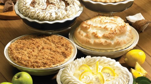 A variety of delicious pies on a wooden table, including cream, meringue, and crumb-topped options.