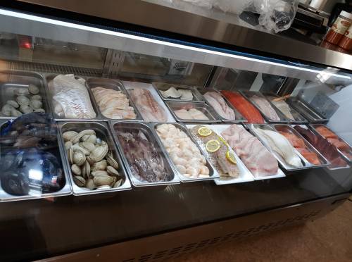 A display case filled with various fresh seafood, including fish, clams, and scallops, arranged in metal trays.