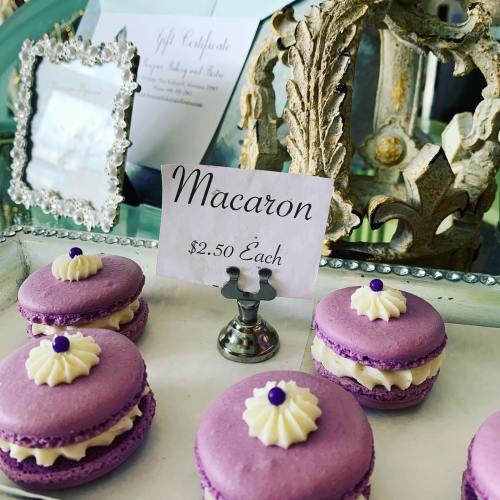 A display of purple macarons with cream filling, priced at $2.50 each, next to a decorative frame and gift certificate.
