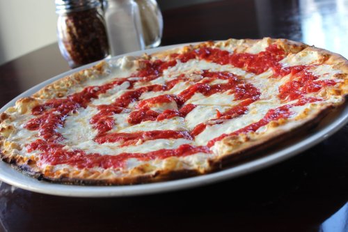 A freshly baked pizza with a thin crust, topped with cheese and a spiral of marinara sauce, served on a white plate.
