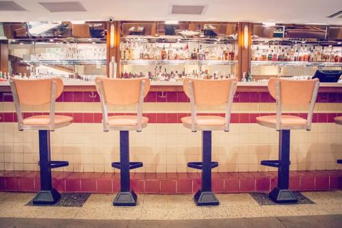 Four empty bar stools lined up in front of a well-stocked bar with shelves of bottles in the background.