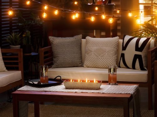 Cozy outdoor seating area with string lights, a table with candles, and drinks on a woven tablecloth.