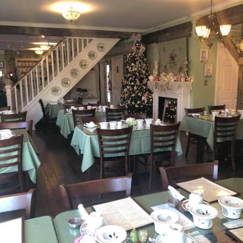 A cozy tea room decorated for the holidays, featuring tables set with tea sets and a Christmas tree in the corner.