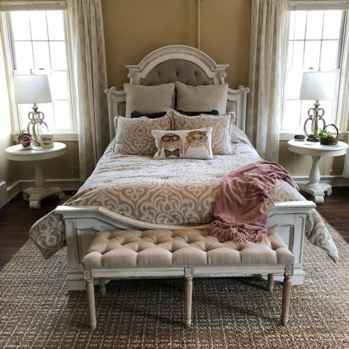 A cozy bedroom featuring a stylish bed with decorative pillows, a tufted bench, and soft lighting from bedside lamps.