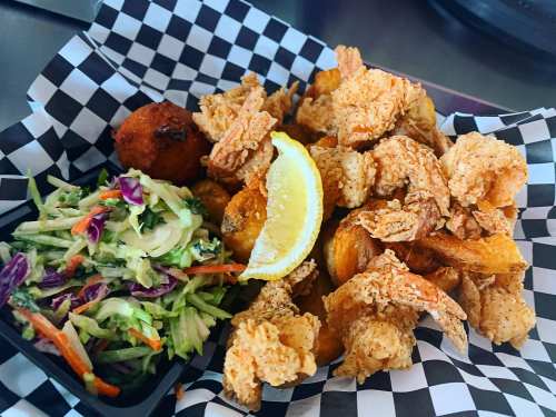 A basket of crispy fried shrimp with a lemon wedge, served alongside coleslaw and a cornbread muffin.