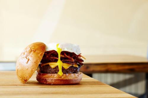 A juicy burger with melted cheese, crispy bacon, and a runny fried egg on a toasted bun, set on a wooden table.
