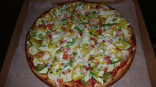 A large pizza topped with cheese, green and yellow peppers, tomatoes, and various vegetables on a golden crust.