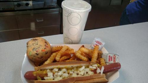 A hot dog with mustard and onions, crinkle fries, a cookie, and a drink in a cup on a table.