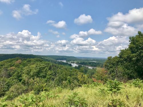 A scenic view of lush green hills and a river under a partly cloudy sky.