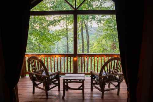 A cozy porch with two wooden chairs and a small table, surrounded by lush green trees and a serene view.