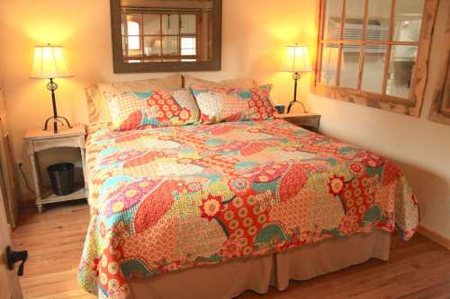 Cozy bedroom with a colorful quilted bedspread, two lamps, and wooden accents.