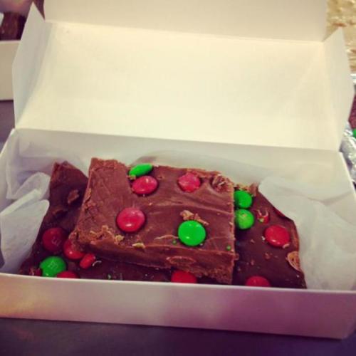 A white box containing chocolate fudge topped with red and green candies.