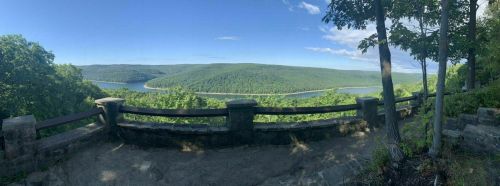 Panoramic view of a lush green landscape with a river winding through, framed by trees and a stone railing.