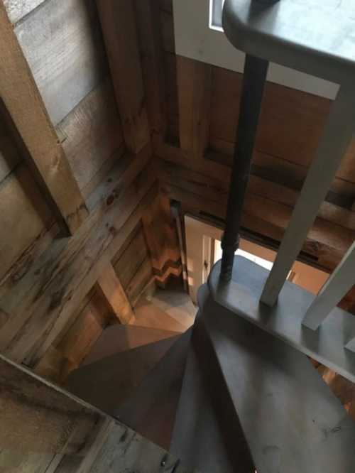 A spiral staircase viewed from above, surrounded by wooden walls and a door at the top.