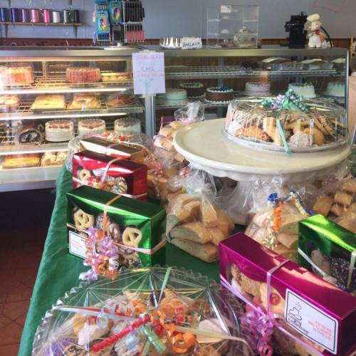 A display of various cakes and pastries in a bakery, with colorful packaging and a glass case in the background.