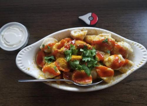 A dish of colorful snacks topped with sauce and cilantro, served with a small container of cream and a Pokéball decoration.