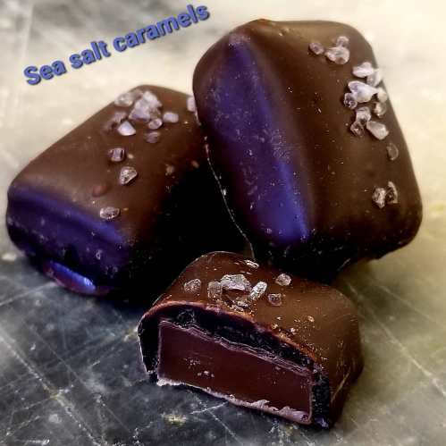 Three dark chocolate sea salt caramels, one cut in half to reveal the gooey center, sprinkled with sea salt.