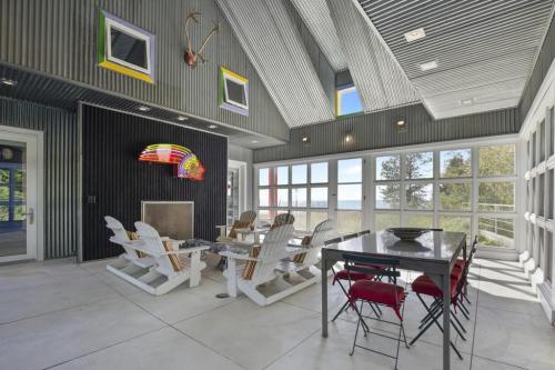 Bright, modern indoor space with a dining table, white chairs, and large windows showcasing a scenic view.