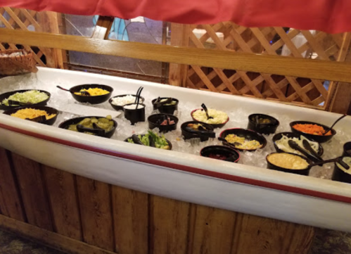 A vintage bathtub filled with ice, holding various bowls of salad toppings and condiments.
