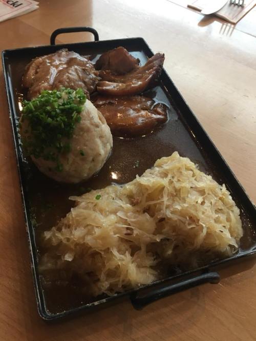 A platter featuring meat, a large dumpling topped with green onions, and a side of sauerkraut in a savory sauce.