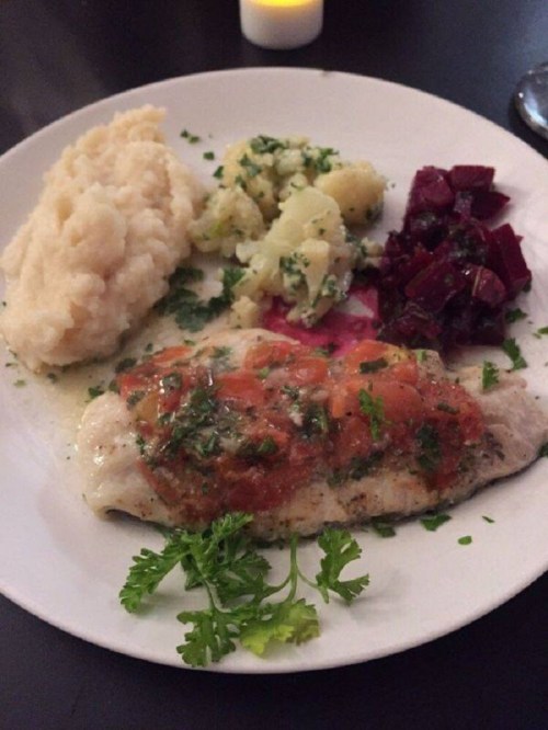 A plate featuring fish with tomato sauce, mashed potatoes, beets, and a sprinkle of herbs.