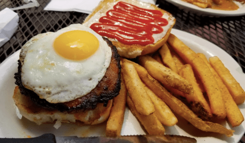 A plate with a sandwich featuring a fried egg and ketchup, alongside a serving of golden French fries.