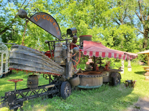 A whimsical, steampunk-inspired food cart with a striped canopy, surrounded by greenery.