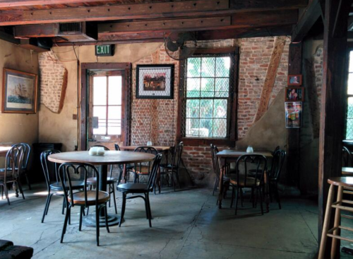Cozy restaurant interior with wooden beams, brick walls, and empty tables near windows.