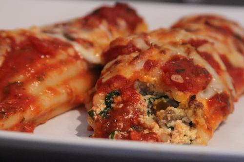 Close-up of stuffed pasta shells topped with marinara sauce and melted cheese on a white plate.