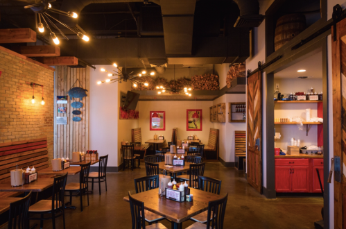 Cozy restaurant interior with wooden tables, black chairs, and warm lighting, featuring rustic decor and a welcoming atmosphere.