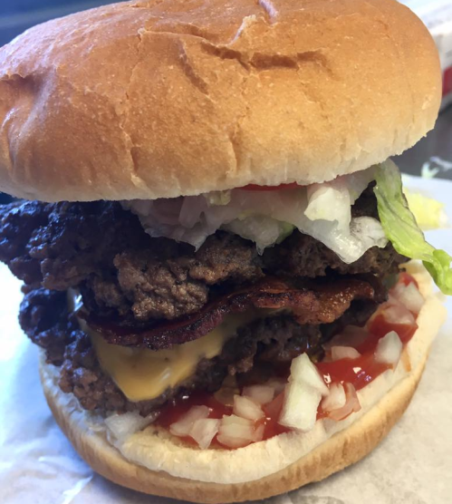 A stacked burger with two beef patties, bacon, cheese, lettuce, tomato, and onions, all in a soft bun.