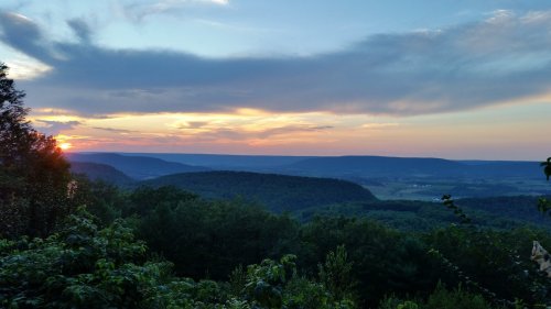 A scenic sunset over rolling hills, with vibrant clouds and lush greenery in the foreground.
