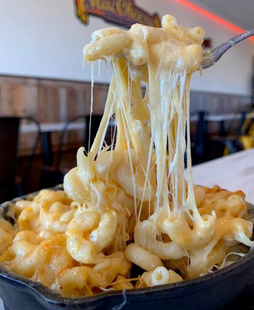 A fork lifting creamy, cheesy macaroni and cheese from a cast-iron dish, showcasing its gooey texture.