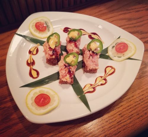 A decorative plate with sushi topped with jalapeños, drizzled with sauces, and garnished with lemon and cherry tomatoes.