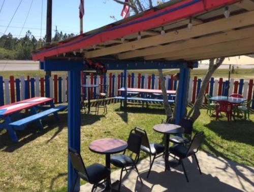 Outdoor seating area with colorful tables and chairs under a covered patio, surrounded by a picket fence.
