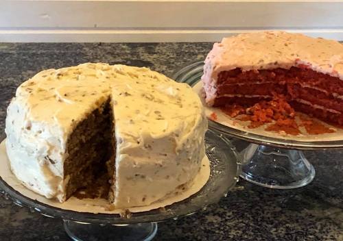 Two layered cakes on glass stands: one with cream frosting and nuts, the other with pink frosting and red layers.
