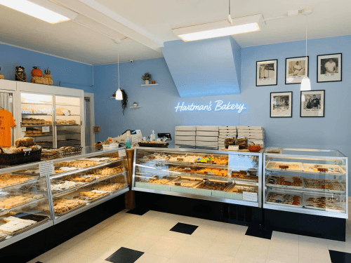 A cozy bakery interior featuring glass display cases filled with various baked goods and a sign that reads "Hartman's Bakery."