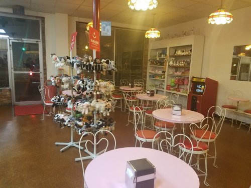 A cozy café with pink tables, white chairs, and a display of stuffed animals in the corner.