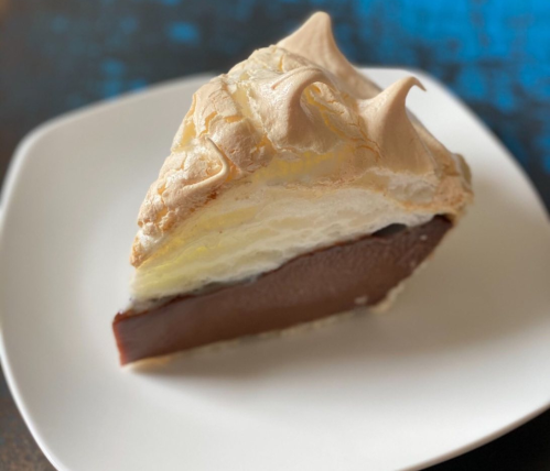 A slice of chocolate pie topped with fluffy meringue on a white plate, set against a blue background.