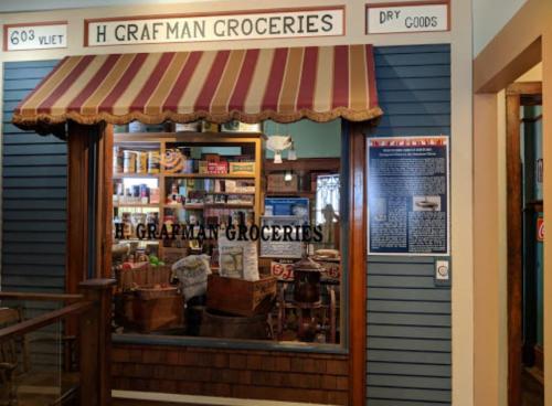 A vintage grocery store display with a striped awning, shelves of goods, and wooden crates inside.