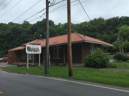A brick building with a red tile roof, featuring a sign that reads "Wabash," surrounded by greenery and power lines.