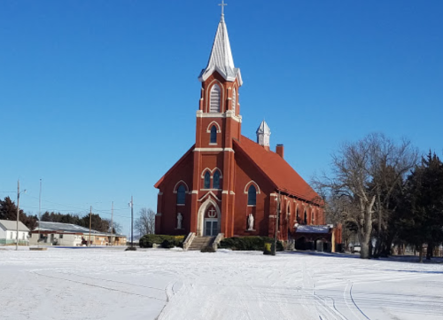 A red brick church with a tall steeple, surrounded by snow, under a clear blue sky.