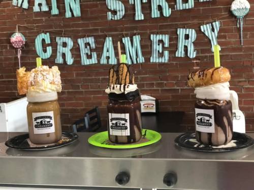 Three extravagant milkshakes topped with whipped cream, pastries, and colorful straws, displayed at a creamery.