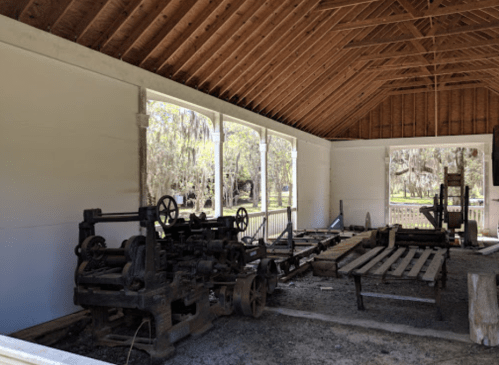 Interior of a rustic building featuring old machinery and wooden beams, surrounded by greenery outside.