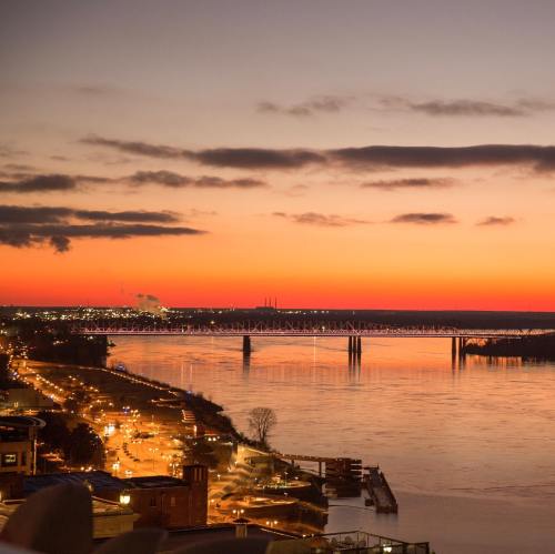 A scenic sunset over a river, with a bridge and city lights reflecting on the water.
